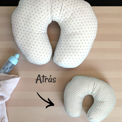 Três almofadas em U com padrões de estrelas e bolinhas, chupeta azul e pano rosa sobre mesa de madeira.