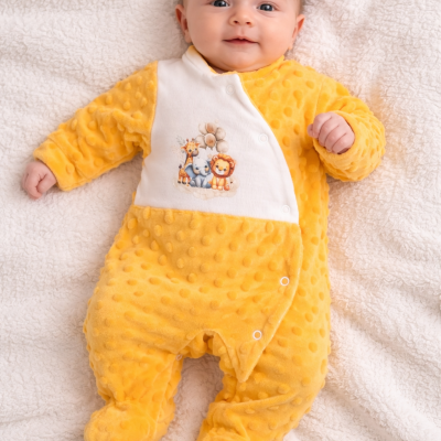 Pijama de bebé amarelo com padrão de bolinhas e estampado de animais sobre manta branca.
