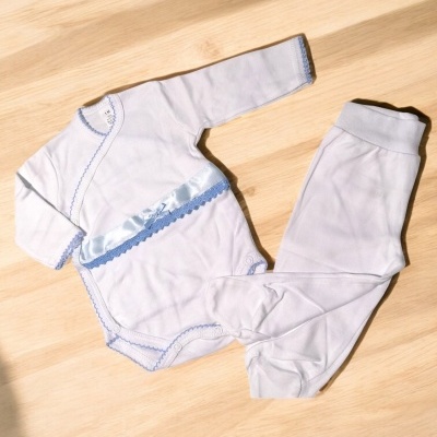 Conjunto de roupa para bebé branco com detalhes azuis sobre madeira clara