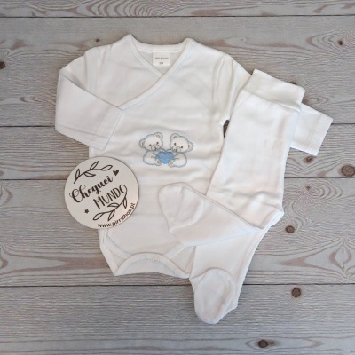 Conjunto bebé branco com bordado de ursos e placa redonda com texto em fundo de madeira.