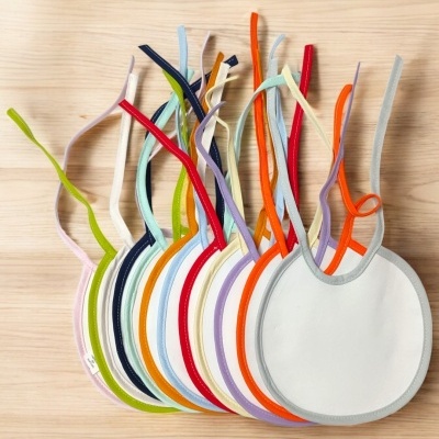 Babetes redondos coloridos para bebé com fitas para amarrar sobre madeira clara