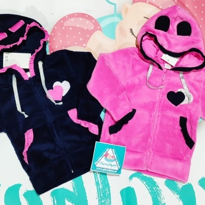 Casacas de bebé felpudas, azul escuro com detalhes cor-de-rosa e rosa com capuz decorado, sobre superfície branca colorida