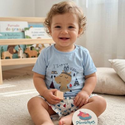 Bebé com t-shirt azul clara e calções estampados a sorrir sentado em tapete