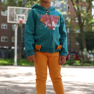 Criança com casaco azul turquesa e calças laranja em parque de basquetebol