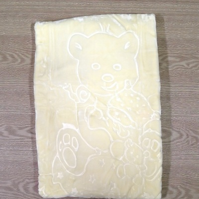 Manta amarela com desenho de urso gravado sobre superfície de madeira.