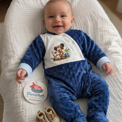 Bebé deitado com macacão azul texturizado com estampa do Mickey e sapatos castanhos ao lado