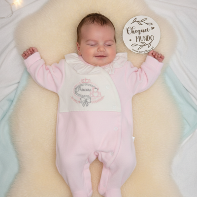 Bebé de macacão rosa e branco a dormir sobre tapete de pelo creme with placa redonda ao lado.