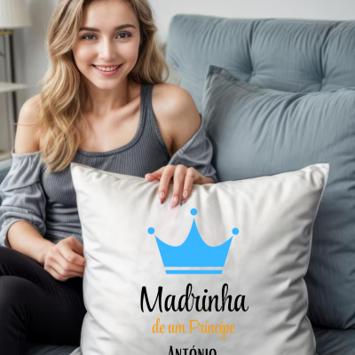 Almofada branca com coroa azul e texto 'Madrinha de um Príncipe ANTÓNIO' numa sala com sofá cinza