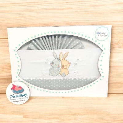 Fralda de bebé branca e cinza com bordado de coelhinhos em embalagem com estrelas verdes