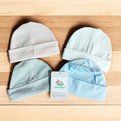 Quatro gorros de bebé em tecidos macios coloridos em tons pastel sobre uma mesa de madeira clara