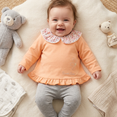 Bebé sorridente deitado com roupa laranja e cinzenta, com peluches ao lado