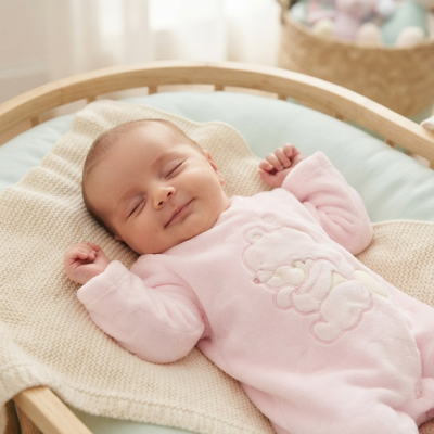 Bebé de pijama rosa de veludo deitado num berço de madeira clara com cobertor bege