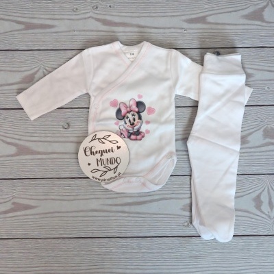 Conjunto de roupas de bebé com body branco e calças brancas no chão cinzento de madeira.