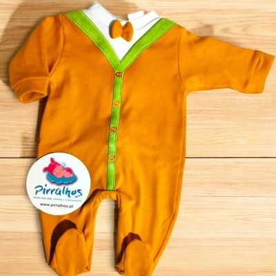 Macacão de bebé laranja com detalhes verdes e branca, etiqueta da marca Pirralhos, sobre fundo de madeira
