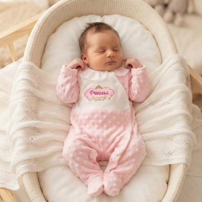 Bebé dormindo numa cesta com fato rosa e babete branco com texto Princesa
