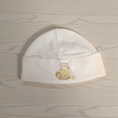 Gorro de bebé branco com estampa de ursinho e pato, sobre madeira clara