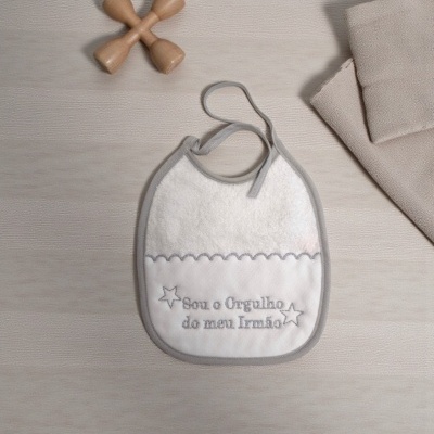 Babete branco com bordado cinzento 'Sou o Orgulho do meu Irmão' sobre superfície de madeira clara