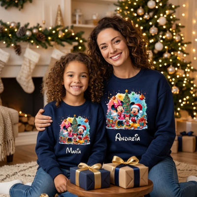 Pai e filha usando sweatshirts azuis com estampas de Natal de Mickey e Minnie e nomes personalizados sentados em sala de Natal com presentes.