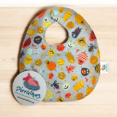 Babete infantil com padrão de monstros coloridos em fundo cinzento