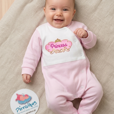 Bebé deitada com macacão rosa e branco com a palavra Princesa e etiqueta Pirralhos no chão.