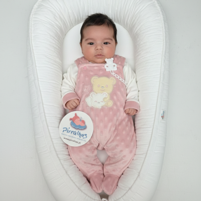 Bebé de pijama rosa com ursinhos bordados deitado numa almofada branca acolchoada