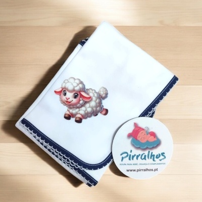 Fralda branca com borda evelho azul escura e bordado de ovelha sobre madeira clara.