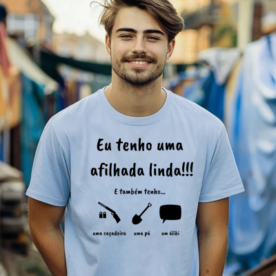 Homem sorridente com camiseta branca escrita em preto 'Eu tenho uma afilhada linda!!! E também tenho... uma caçadeira uma pá um álibi'