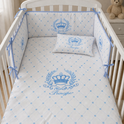 Berço branco com roupa de cama branca e azul decorada com coroas e padrão xadrez