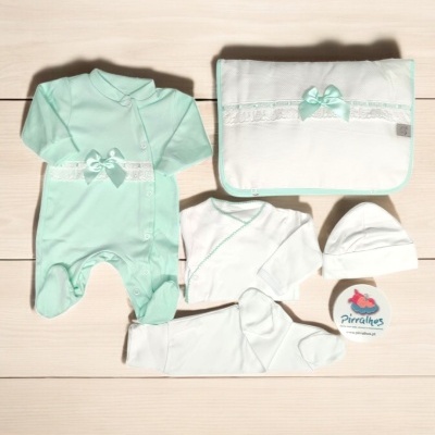 Conjunto de roupa de bebé verde menta e branco com laço e renda sobre piso claro.