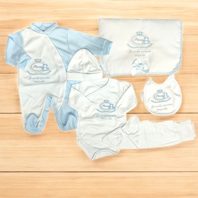 Conjunto de roupa para bebé azul claro e branco com bordados e manta sobre superfície de madeira clara