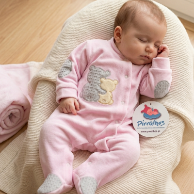 Bebé com macacão rosa com ursinhos, numa almofada bege acolchoada.