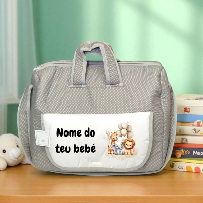 Mala cinzenta de tecido com bolso branco estampado com animais e texto, em mesa de madeira com peluche e livros.