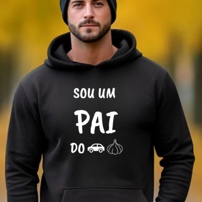 Homem com sweatshirt preta com texto 'SOU UM PAI DO' e emojis de carro e alho, gorro preto e fundo amarelo desfocado.