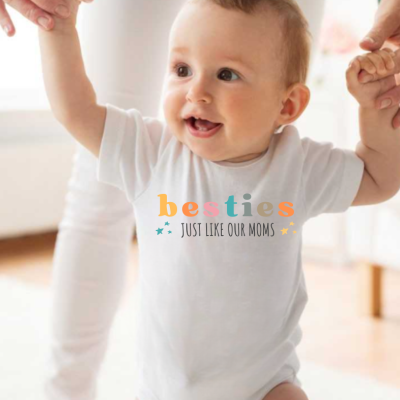 Bebé com camisola branca estampada com texto colorido a ser ajudado a andar