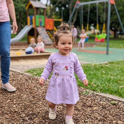 Menina pequena com vestido lilás num parque infantil com escorrega e baloiços