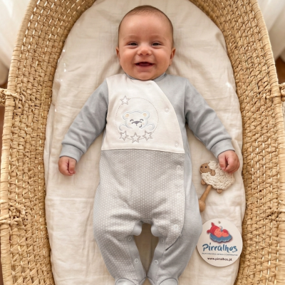Bebé numa alcofa com vestido cinza e branco e chocalho de ovelha
