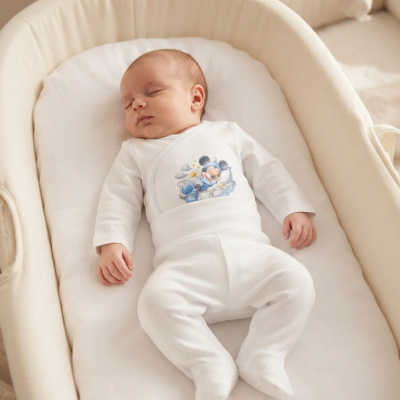 Bebé a dormir num berço creme com pijama branco e estampado do Mickey azul.