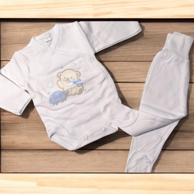 Conjunto de roupa de bebé branco com ursinho e carrinho azul sobre madeira clara