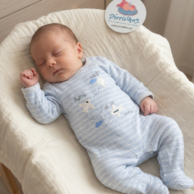 Bebé a dormir com fato de pijama azul claro às riscas e almofada creme.