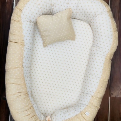 Ninho e almofada de bebé bege e branco com padrão de estrelas, sobre chão de madeira escura