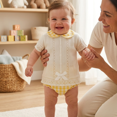 Bebé vestindo body amarelo e camisola de malha creme com mulher a segurá-lo num quarto infantilm