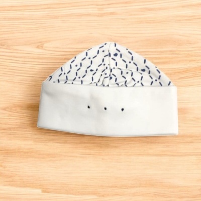 Gorro branco com padrão azul escuro sobre madeira clara