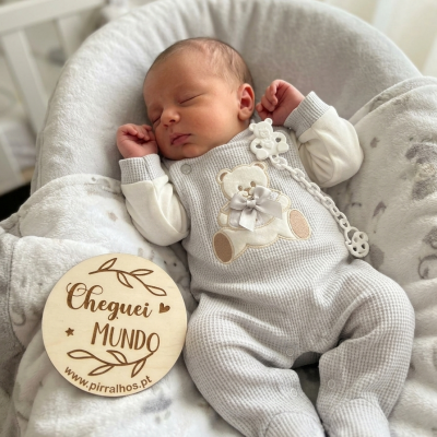 Bebé a dormir vestido com fato cinzento claro com ursinho, em almofada cinzenta com círculo de madeira Cheguei MUNDO.