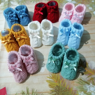 Dez pares de sapatinhos de bebé em malha colorida com fitas de cetim, sobre superfície clara com folhas decorativas