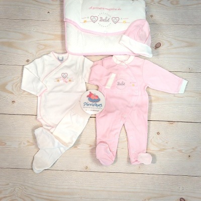Conjunto bebé rosa e branco com body, pijama, gorro e manta bordada sobre madeira clara