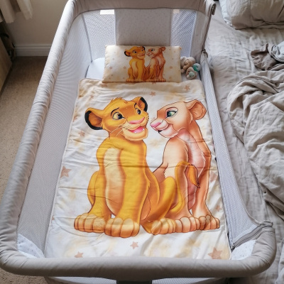 Berço branco com edredão e almofada com personagens de leões amarelos e cor de rosa.