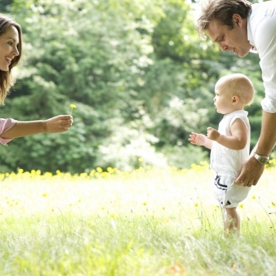 Bebé a dar primeiros passos ao ar livre entre adultos