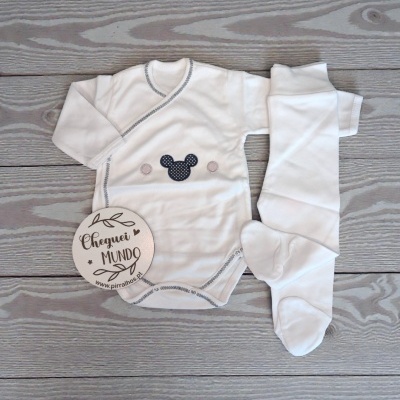 Conjunto de bebé branco com padrão e figura de orelhas pretas sobre fundo de madeira cinza.