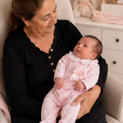 Bebé vestido com macacão rosa ao colo de mulher com camisola preta numa cadeira creme