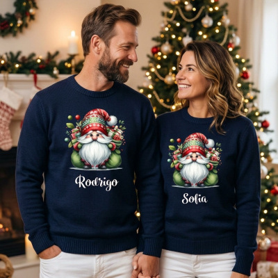 Casal com camisolas de Natal personalizadas em azul-marinho com duendes e nomes, árvore de Natal iluminada ao fundo
